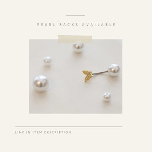 May include: A belly button ring with a gold-colored, leaf-shaped charm and a large white pearl. The image also shows several loose white pearls of varying sizes. Text reads "PEARL BACKS AVAILABLE" and "LINK IN ITEM DESCRIPTION."