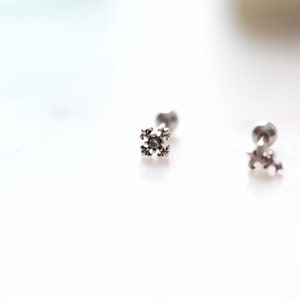 May include: Close-up of three silver-colored stud earrings. Each earring features a small, decorative, four-pointed design. The earrings are set against a bright, white background, highlighting their intricate details and metallic sheen.