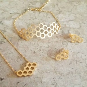May include: A gold-colored jewelry set featuring a honeycomb design. The set includes a necklace, bracelet, and a pair of stud earrings. The jewelry is displayed on a light-colored surface.