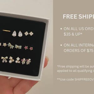 May include: A collection of gold-toned stud earrings in a black box. The earrings feature various designs, including stars, bows, teardrops, and floral shapes. The text "FREE SHIPPING" is visible on the right side of the image.