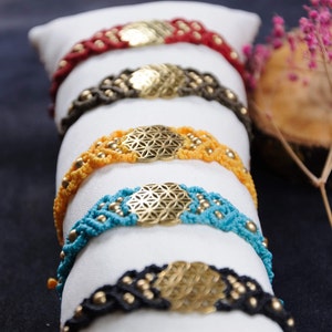 Puede incluir: Cinco pulseras con un dije de flor de la vida. Las pulseras están hechas de macramé y tienen cuentas de diferentes colores. Los colores son rojo, marrón, amarillo, azul y negro.