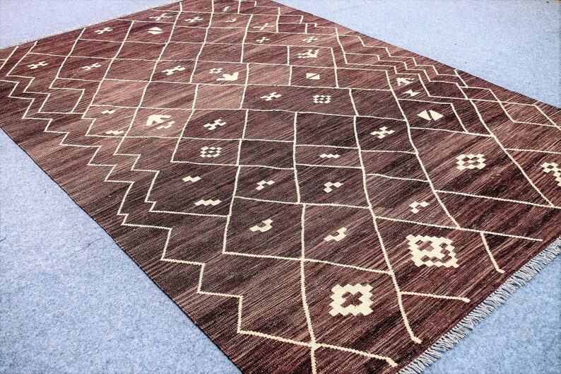 May include: A brown and white geometric patterned rug with a fringe border. The rug has a traditional Moroccan design.