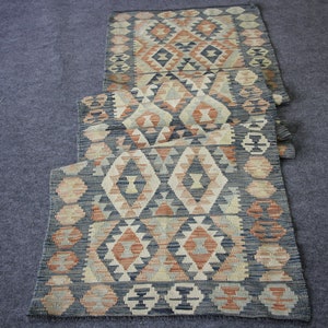 May include: A long, narrow rug with a geometric pattern in shades of blue, beige, and orange. The rug is made of woven fabric and has a traditional design.
