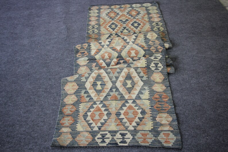 May include: A long, narrow rug with a geometric pattern in shades of blue, beige, and orange. The rug is made of woven fabric and has a traditional design.