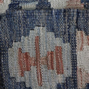 May include: Close-up of a woven rug with a geometric pattern in shades of blue, white, and red.