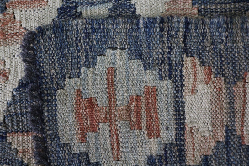 May include: Close-up of a woven rug with a geometric pattern in shades of blue, white, and red.