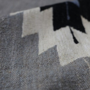 May include: Close-up of a grey and white woven rug with a geometric pattern. The rug has a textured surface and is made of natural fibres.