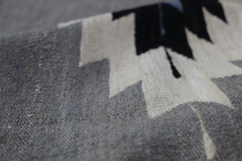 May include: Close-up of a grey and white woven rug with a geometric pattern. The rug has a textured surface and is made of natural fibres.