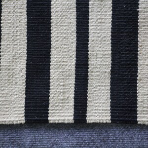 May include: A black and white striped rug with a blue fabric underneath. The rug is made of woven fabric and has a textured surface.