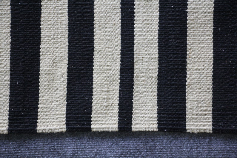 May include: A black and white striped rug with a blue fabric underneath. The rug is made of woven fabric and has a textured surface.
