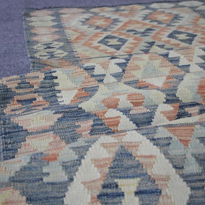 May include: A folded rug with a geometric pattern in shades of blue, white, and pink.