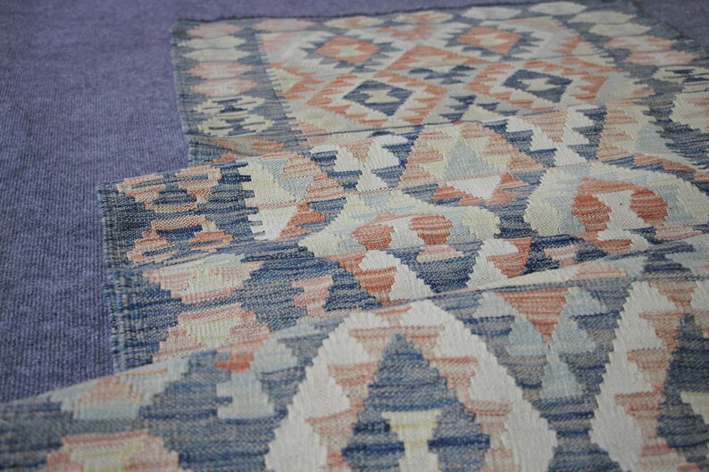 May include: A folded rug with a geometric pattern in shades of blue, white, and pink.