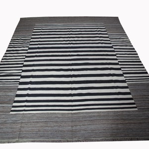 May include: A black and white striped rug with a gray border. The rug has a contemporary design and is made of wool.