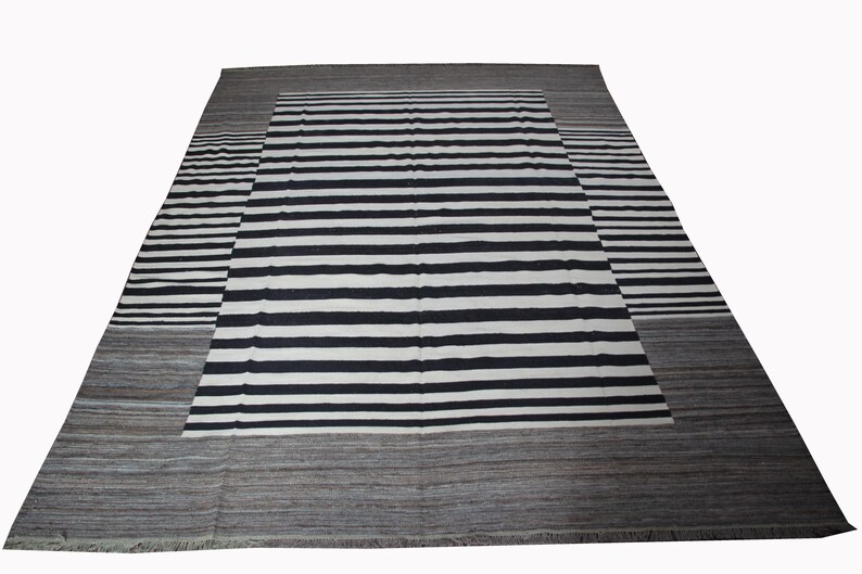 May include: A black and white striped rug with a gray border. The rug has a contemporary design and is made of wool.
