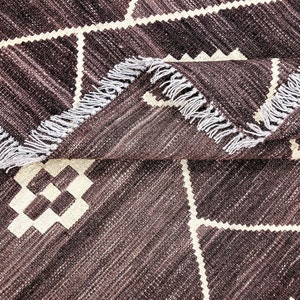 May include: A brown and white patterned rug with a fringe border. The rug has a geometric design with white squares and diamonds on a brown background.