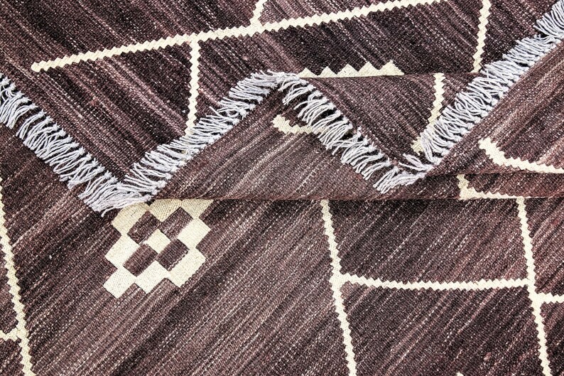 May include: A brown and white patterned rug with a fringe border. The rug has a geometric design with white squares and diamonds on a brown background.