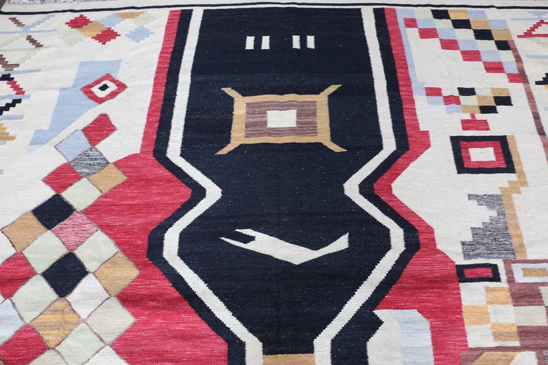 Puede incluir: Una alfombra colorida con un patr&oacute;n geom&eacute;trico. La alfombra tiene un centro negro con un dise&ntilde;o blanco y est&aacute; rodeada de formas geom&eacute;tricas rojas, blancas y azules.