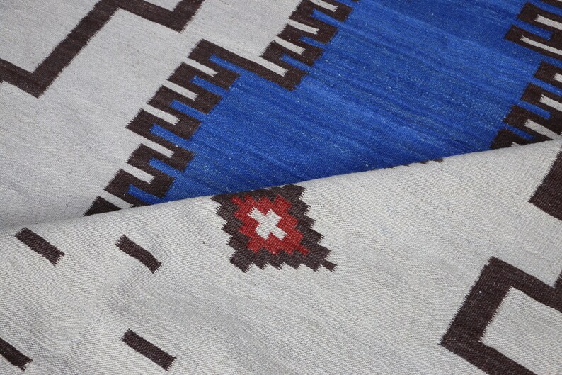 May include: A close-up of a white and blue patterned rug with a red and white diamond shape in the center. The rug has a geometric design with black lines.