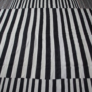 May include: Black and white striped rug with a woven texture. The rug is made of natural fibers and has a simple, modern design.