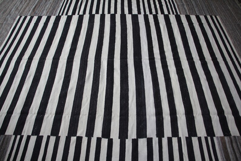 May include: Black and white striped rug with a woven texture. The rug is made of natural fibers and has a simple, modern design.