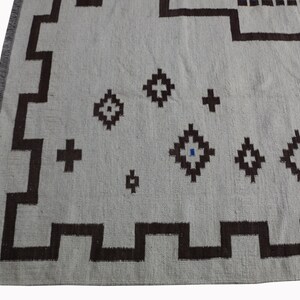 May include: A white rug with a geometric pattern in brown and blue. The rug has a fringe border.