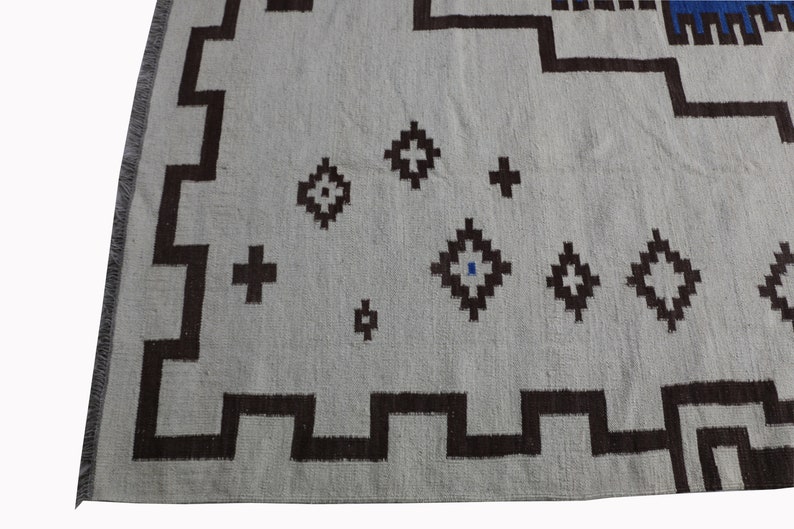 May include: A white rug with a geometric pattern in brown and blue. The rug has a fringe border.