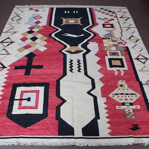 Puede incluir: Una alfombra con estampado geom&eacute;trico en un esquema de colores rojo, negro y blanco. La alfombra tiene un dise&ntilde;o central con un patr&oacute;n en blanco y negro y un patr&oacute;n en rojo y blanco a cada lado.
