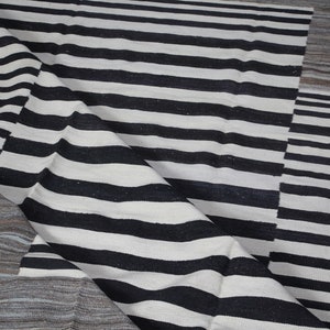 May include: Black and white striped rug with a textured woven design. The rug has a geometric pattern with a folded edge.