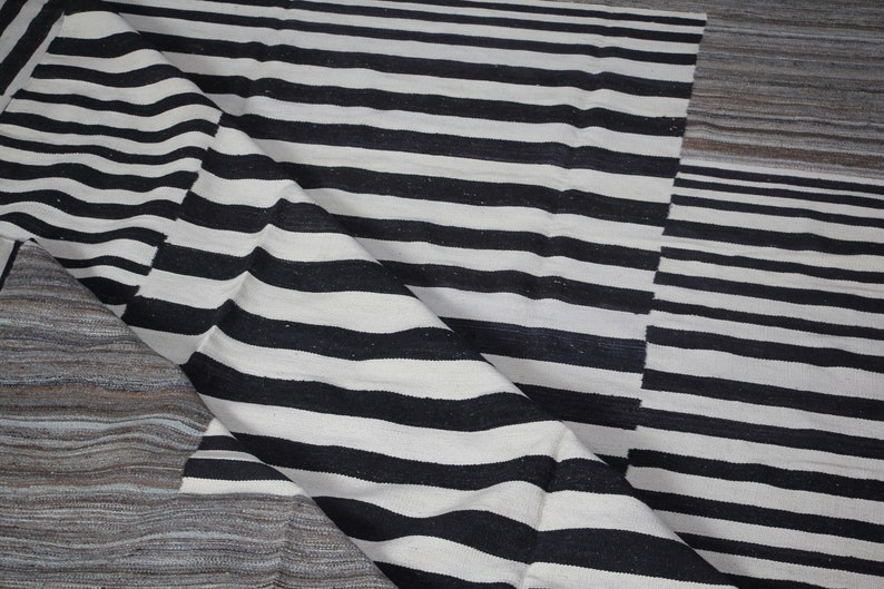 May include: Black and white striped rug with a textured woven design. The rug has a geometric pattern with a folded edge.
