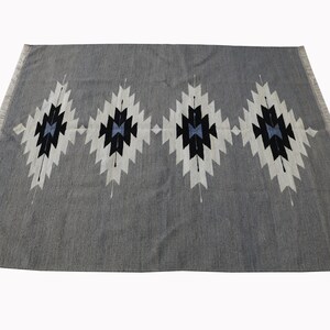 May include: A grey rug with a geometric pattern in white, black, and blue. The pattern features four diamond shapes with a central star design.