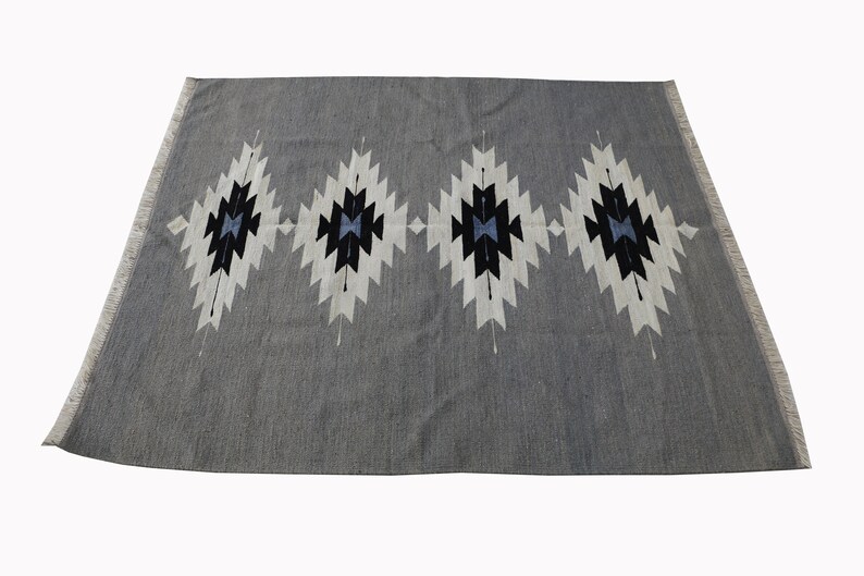 May include: A grey rug with a geometric pattern in white, black, and blue. The pattern features four diamond shapes with a central star design.