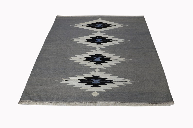 May include: A grey rug with a white and black geometric pattern. The rug has a fringed border.