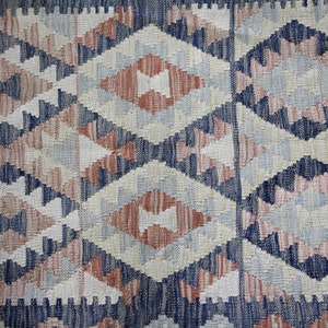 May include: A close-up of a woven rug with a geometric pattern in shades of blue, pink, and white.
