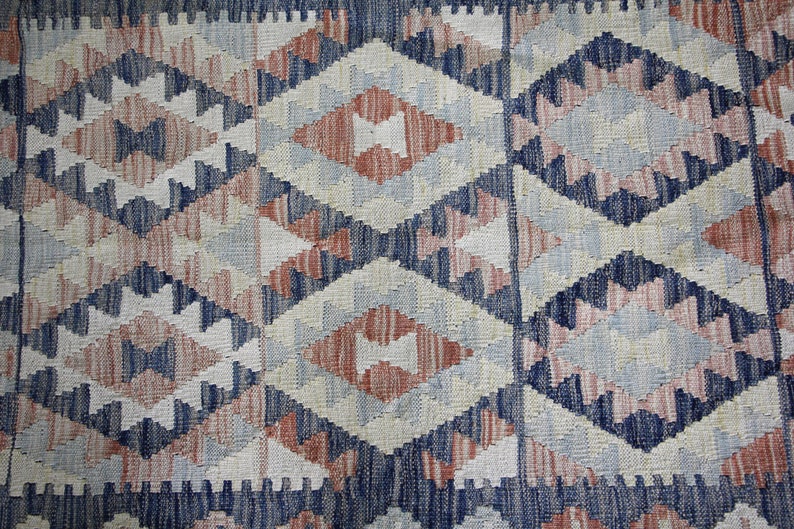 May include: A close-up of a woven rug with a geometric pattern in shades of blue, pink, and white.