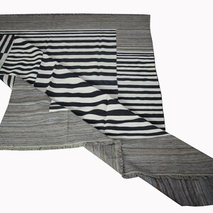 May include: A black and white striped rug with a gray border. The rug is folded in half and the stripes are visible on both sides.