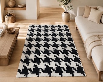 Puede incluir: Una alfombra rectangular con un patrón de pata de gallo en blanco y negro de alto contraste. La alfombra está colocada sobre un suelo de madera clara, mostrando un diseño geométrico repetitivo que cubre toda la superficie del tapete.