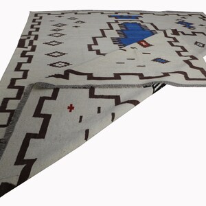 May include: A white rug with a brown and blue geometric pattern. The rug is folded in half and the pattern is visible on both sides.