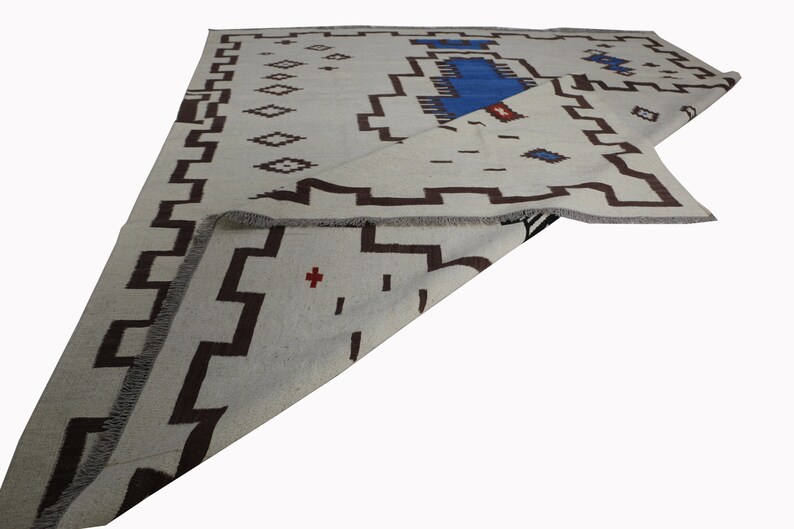 May include: A white rug with a brown and blue geometric pattern. The rug is folded in half and the pattern is visible on both sides.