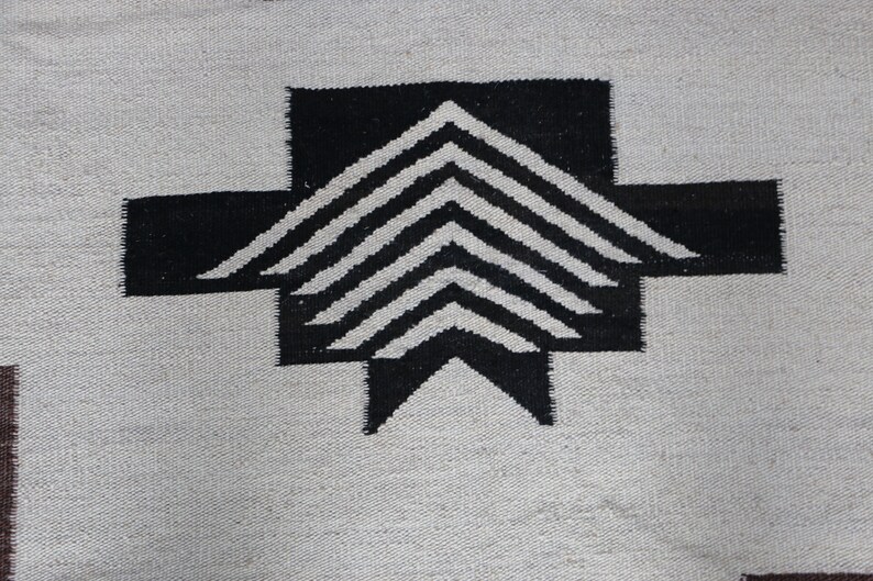 May include: Black and white geometric pattern woven into a rug. The pattern features a series of overlapping triangles.