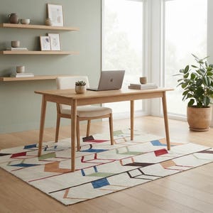 May include: A rectangular light wood desk with four tapered legs and a matching upholstered chair. The desk holds a laptop, a small potted succulent, and a stack of books. A cream-colored area rug features a geometric pattern in blue, red, and green.