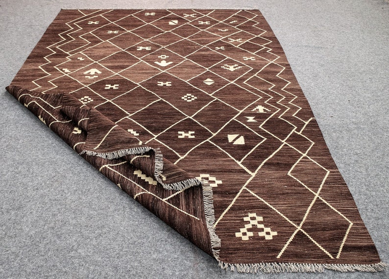 May include: A brown and cream patterned rug with a geometric design. The rug has a fringe border.