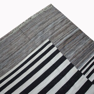 May include: A black and white striped rug with a gray border. The rug has a geometric pattern and is made of wool.