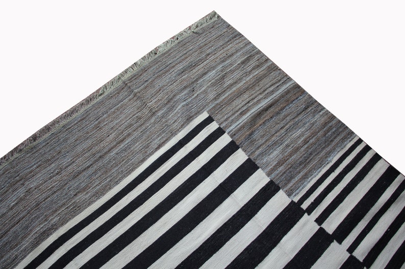 May include: A black and white striped rug with a gray border. The rug has a geometric pattern and is made of wool.