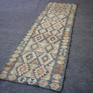 May include: A long, narrow rug with a geometric pattern in shades of brown, beige, and black. The rug has a traditional, hand-woven look.