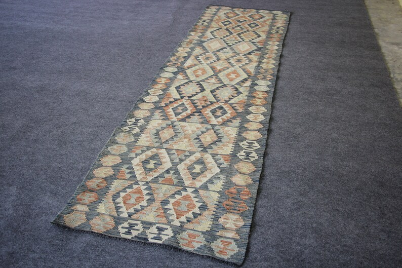 May include: A long, narrow rug with a geometric pattern in shades of brown, beige, and black. The rug has a traditional, hand-woven look.