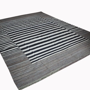 May include: A black and white striped rug with a gray border. The rug has a fringe around the edges.