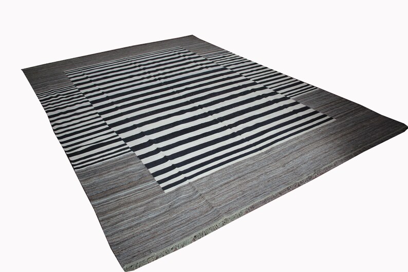 May include: A black and white striped rug with a gray border. The rug has a fringe around the edges.