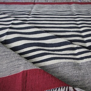 May include: A black and white striped throw blanket with a red border and fringe. The blanket is folded in half and the stripes are visible.