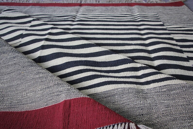 May include: A black and white striped throw blanket with a red border and fringe. The blanket is folded in half and the stripes are visible.