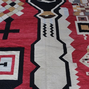 Puede incluir: Una alfombra roja, blanca y negra con un patr&oacute;n geom&eacute;trico de dise&ntilde;o tradicional. La alfombra tiene una variedad de formas y patrones, incluyendo cuadrados, diamantes y zigzags.